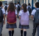 Estudiantes caminan hacia su escuela con mochilas.
