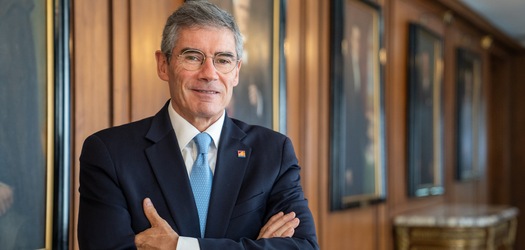 Hombre con traje azul y corbata celeste, de pie con los brazos cruzados